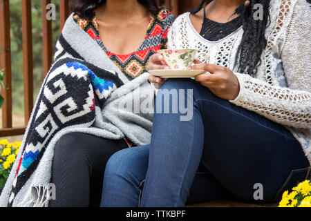 Midsection of woman holding boire lors d'un entretien avec sœur on porch Banque D'Images