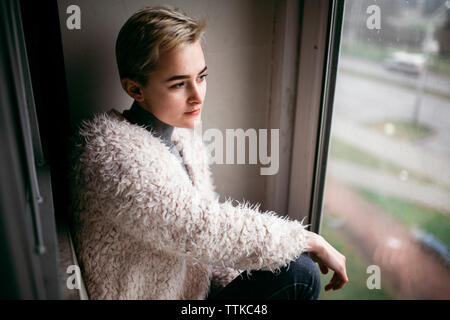 Femme sérieuse à la recherche d'une fenêtre tout en restant assis à la maison Banque D'Images