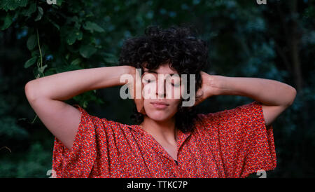 Close-up of woman with hands couvrant les oreilles debout contre des arbres en parc Banque D'Images