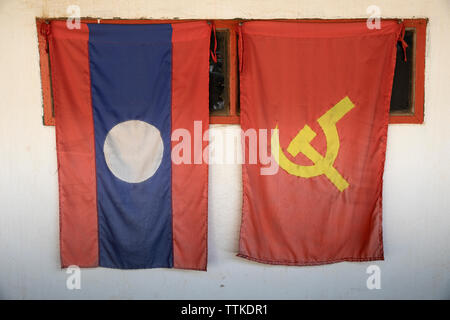 Laos drapeau national et le Parti Populaire Révolutionnaire Lao (PPRL) drapeau accroché à partir de la vitrine, Nong Khiaw, Muang District Ngoi, Luang Prabang Provi Banque D'Images