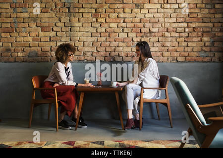 Smiling businesswomen talking while sitting at table in hotel lobby Banque D'Images