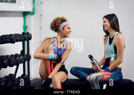 Heureux les athlètes féminins de parler tout en sitting on bench at gym Banque D'Images