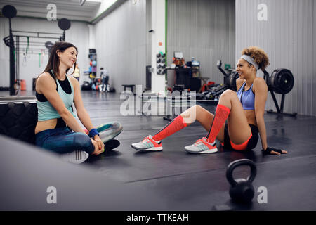 Heureux les athlètes féminins de parler tout en sitting on floor at gym Banque D'Images