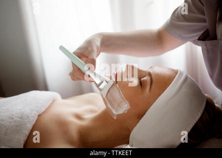 Au milieu de l'application de masque facial thérapeute sur femme à spa Banque D'Images