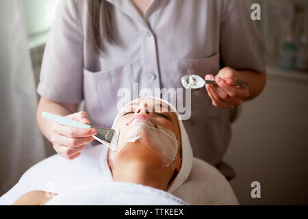 Female therapist appliquant le masque facial sur femme à spa Banque D'Images