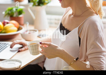 Midsection of woman holding coffee en utilisant un ordinateur portable tout en étant assis à table Banque D'Images