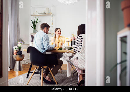 Les femmes sourire soulevant des toasts alors qu'il était assis avec des amis à table à manger Banque D'Images