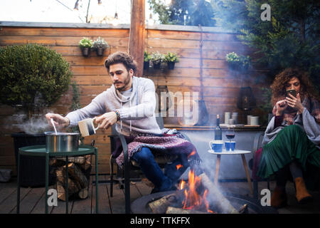 La prise de l'homme tandis que les femmes ami à l'aide de téléphone mobile par fire pit in backyard Banque D'Images