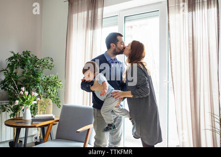 Man carrying son tandis que les baisers femme par fenêtre à la maison Banque D'Images