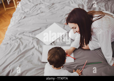 Portrait of happy mother and baby boy avec des fournitures scolaires sur le lit chez lui Banque D'Images