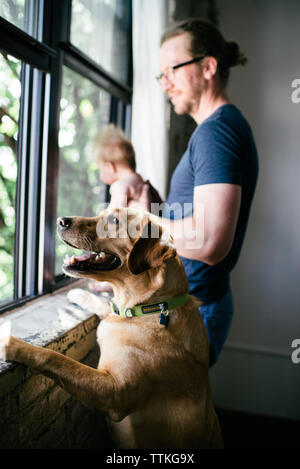 Vue latérale du père avec sa fille et son chien à la recherche d'une fenêtre Banque D'Images