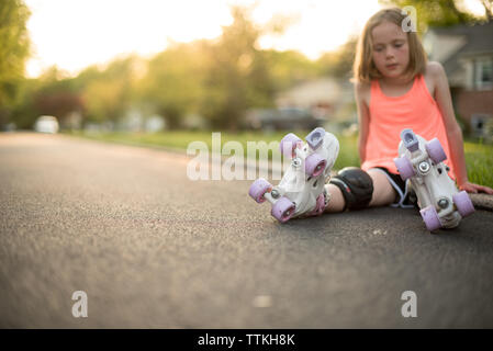 Girl wearing patins à assis sur road at park Banque D'Images