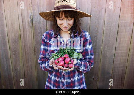 Smiling young female farmer holding radishes debout contre la barrière en bois Banque D'Images