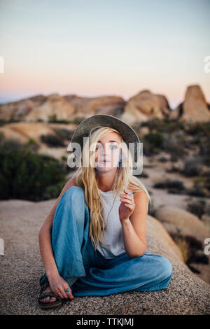 Portrait de femme fumant alors qu'il était assis sur la roche à Joshua Tree National Park Banque D'Images