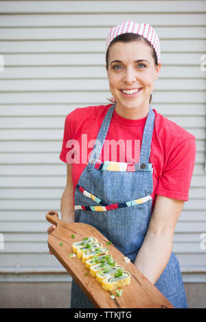 Portrait of smiling chef holding food sur le service à bord tout en se tenant dans une cuisine commerciale Banque D'Images