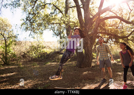 Family smiling girl playing on rope swing in forest Banque D'Images