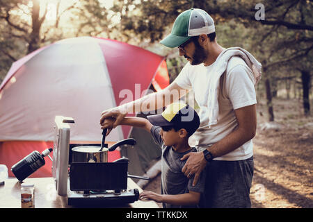 Père et fils la préparation des aliments sur réchaud de camping en forêt Banque D'Images