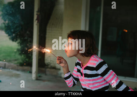 Girl blowing burning sparkler tout en jouant dans la cour Banque D'Images