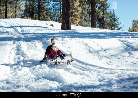 Père et fille de la luge sur le terrain couvert de neige dans la forêt Banque D'Images