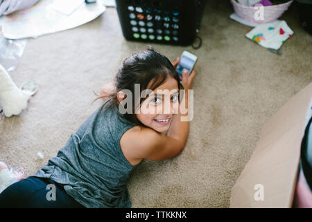 High angle portrait of girl using smart phone en position couchée sur un tapis à la maison Banque D'Images