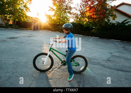 Boy wearing casque de vélo tout en vélo pendant le coucher du soleil Banque D'Images