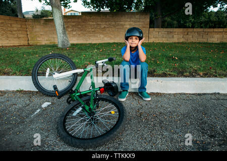 Portrait of boy wearing cycling helmet, assis sur un mur en vélo au parc Banque D'Images