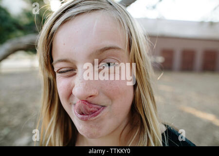 Close-up portrait of playful girl sticking out tongue tout en clignant de l'oeil à la ferme Banque D'Images