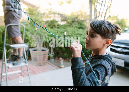 Fils aidant le père à accrocher des lumières de chaîne colorées pendant noël Banque D'Images