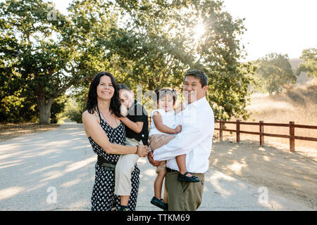 Portrait of happy parents transportant des enfants mignons alors que l'article sur la route contre des arbres en parc Banque D'Images