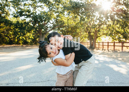 Portrait of cute sœurs embrassant tout en se tenant sur la route contre des arbres en parc Banque D'Images