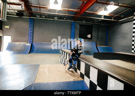 Petit garçon s'assied tout en maintenant son skateboard en skatepark Banque D'Images