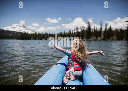 Vue arrière du carefree girl with arms outstretched assis en radeau sur le lac Banque D'Images