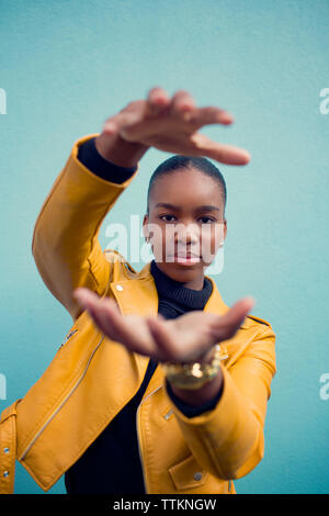 Portrait of young woman gesturing while standing contre mur bleu Banque D'Images