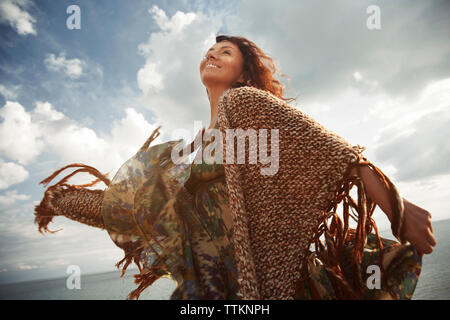 Low angle view of happy woman dancing par mer contre ciel nuageux Banque D'Images