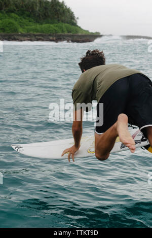 Vue arrière du jeune homme surf en mer Banque D'Images