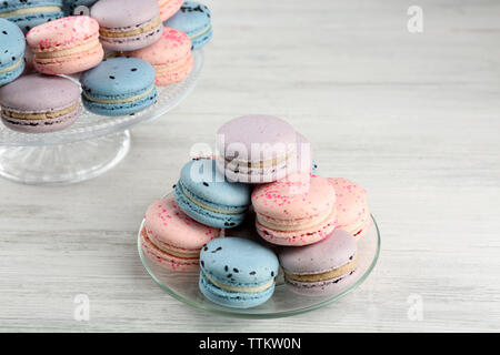 Délicieux macarons sur plaque de verre et sur table en bois Banque D'Images