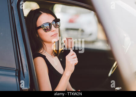 Jeune femme portant des lunettes de soleil sucrés surgelés holding while sitting in car vu à travers la vitre Banque D'Images