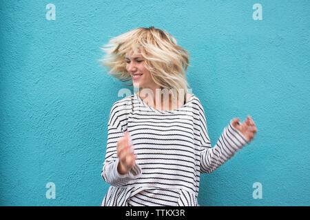 Cheerful young woman tossing cheveux contre mur bleu Banque D'Images