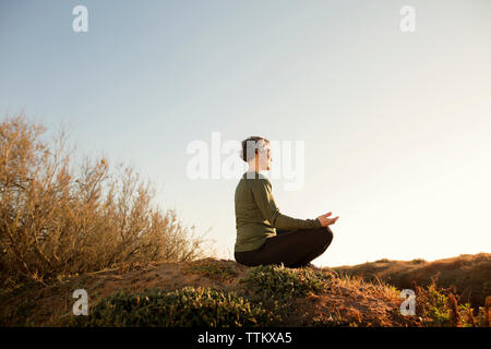 Woman meditating on top of rock against clear sky Banque D'Images