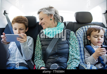 Senior woman looking at grandson using smart phone in car Banque D'Images