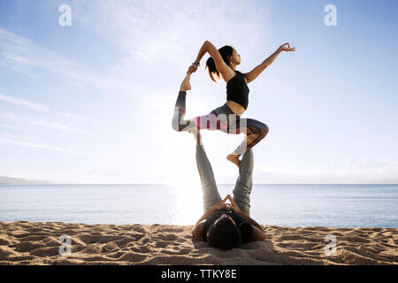 Couple doing yoga on beach against sky Banque D'Images