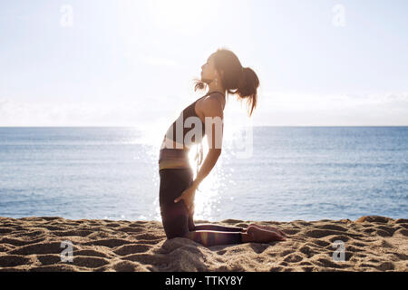 Vue de côté de femme déterminée faisant du yoga sur la plage en été Banque D'Images