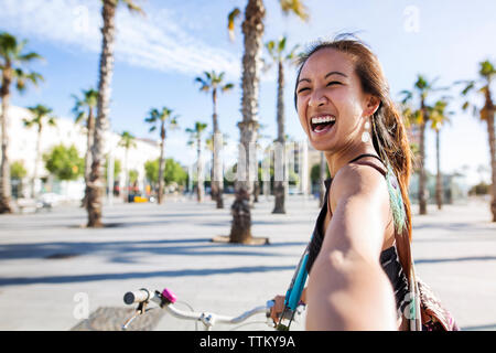 Portrait of cheerful woman riding bicycle sur route au cours de l'été Banque D'Images