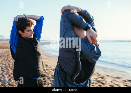 Père et fils d'armes d'étirement en position debout face à face à beach Banque D'Images