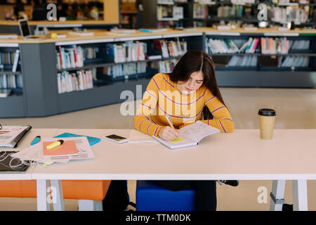 High angle view of woman writing while sitting at table in library Banque D'Images