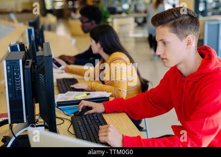 Des amis à l'aide d'ordinateurs de bureau assis à table in library Banque D'Images