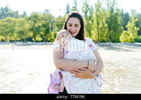 Mère portant mignon fille tout en se tenant dans les arbres contre la mer Banque D'Images