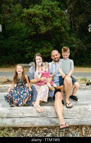 Portrait of happy parents avec enfants mignon assis sur log contre des arbres Banque D'Images