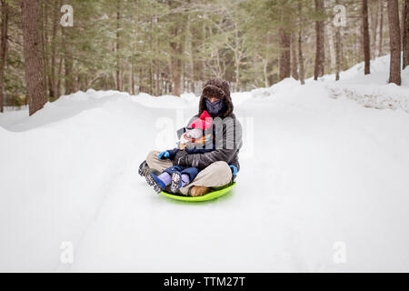 Père assis avec sa fille sur un traîneau au champ couvert de neige Banque D'Images