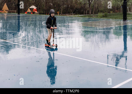 Toute la longueur de boy riding scooter push sur humide de basket-ball pendant la saison des pluies Banque D'Images